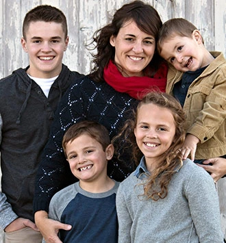 Family of five smiling together for portrait against white wooden backdrop.