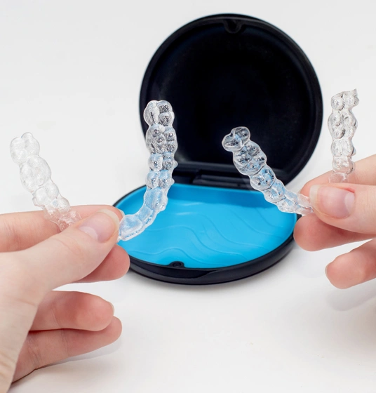 Person holding clear orthodontic retainer with blue gel base against white background.
