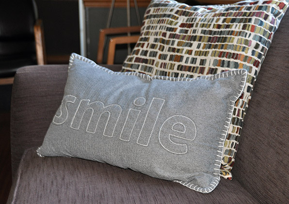Gray decorative pillow with "smile" text on modern couch with patterned pillows.