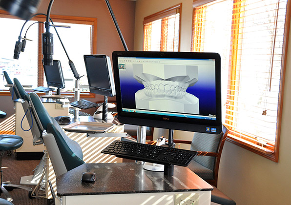 Orthodontic office workspace with computer monitor displaying dental imagery and professional equipment.
