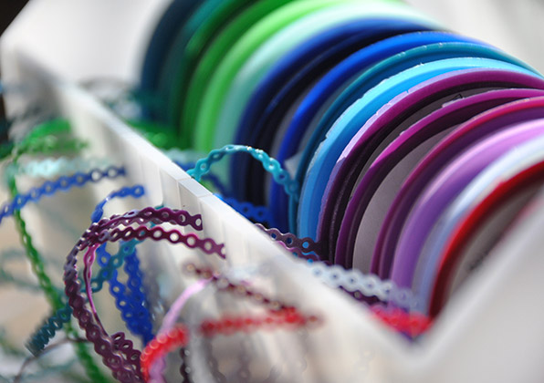 Colorful orthodontic rubber bands and wire arranged on white surface for dental treatment options.
