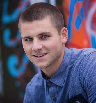 Young man smiling at camera wearing blue shirt against colorful graffiti background.