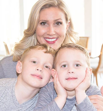 Woman with two young children smiling together in bright, modern indoor setting.