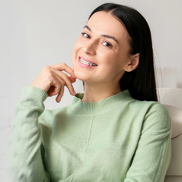 Smiling woman in green sweater touching her face against white background, orthodontics context.