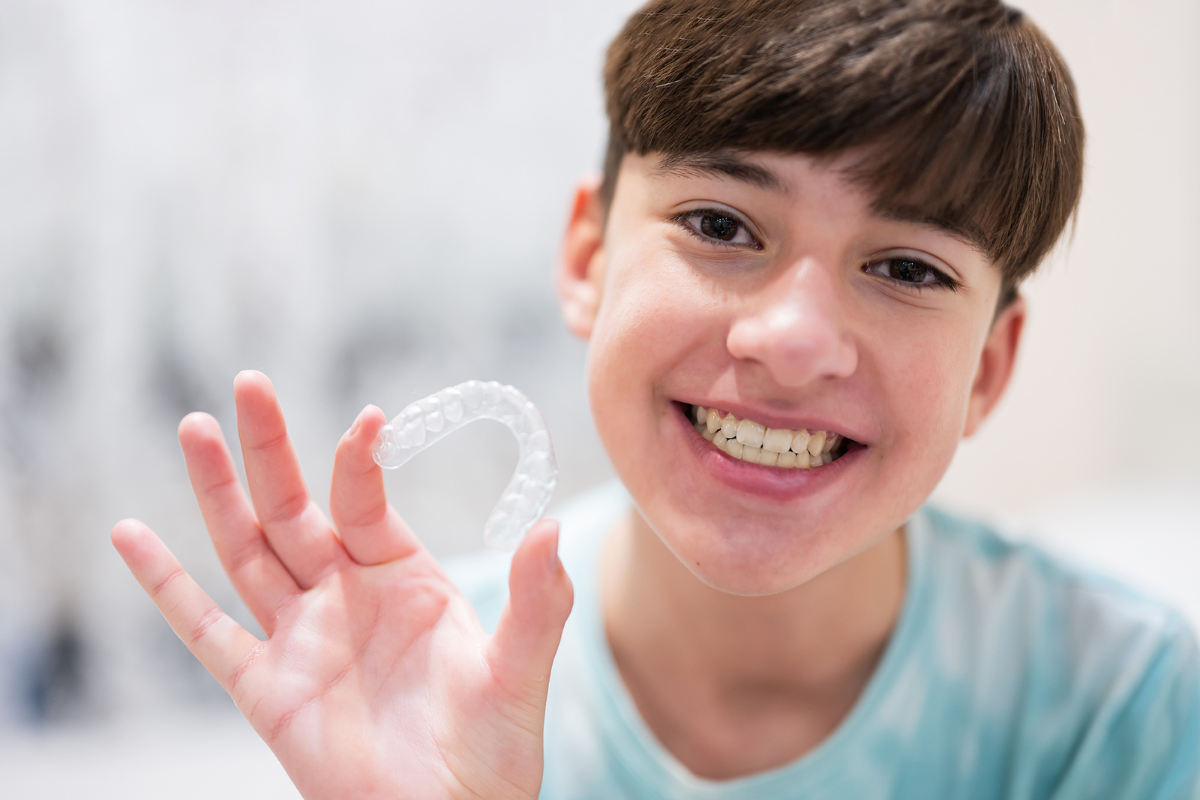 Happy teen holding clear Invisalign aligner and smiling about sports-friendly orthodontic treatment.
