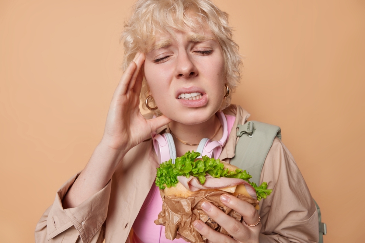 Child experiencing jaw pain while holding a sandwich, illustrating TMJ symptoms.