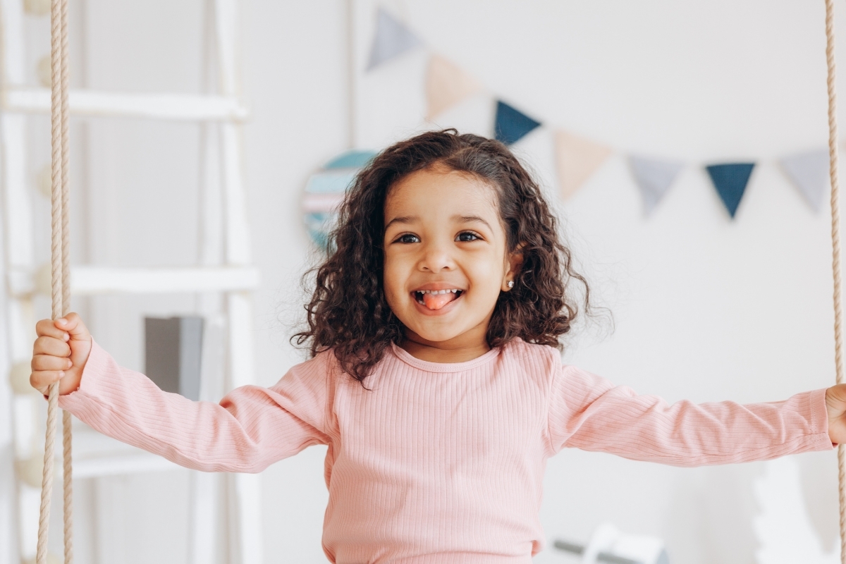 Happy child in pink shirt holding rope swing, smiling brightly.